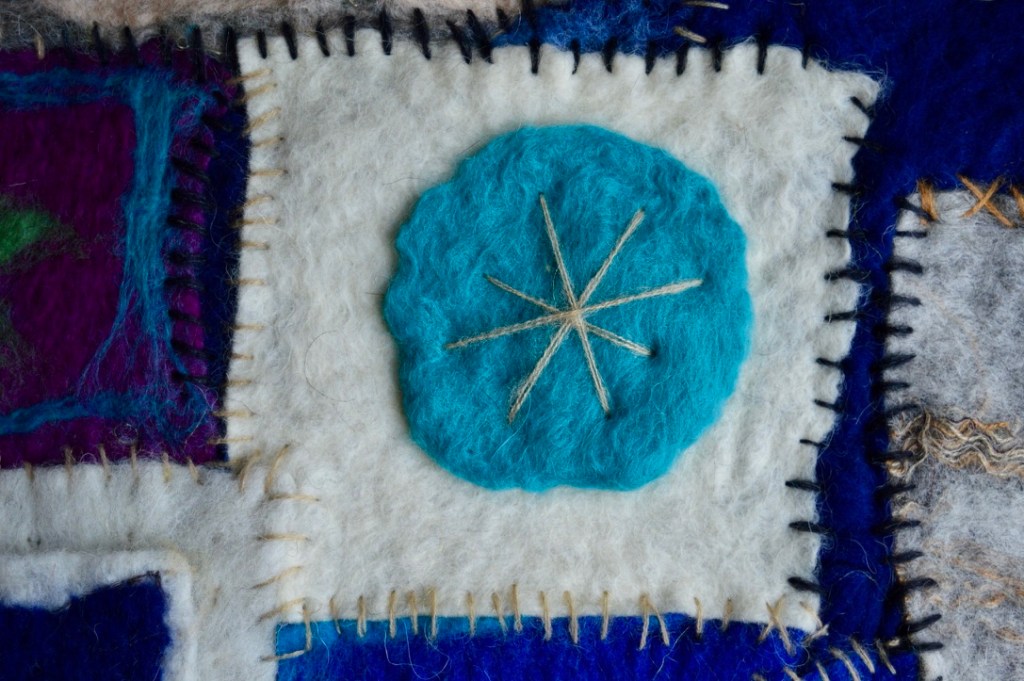 Geometric felt collage inspired by Persian garden design and nomadic architecture, featuring stitched squares in deep blue, white, and violet, with circular felt motifs and layered textures suggesting ornamental balance and modular construction.