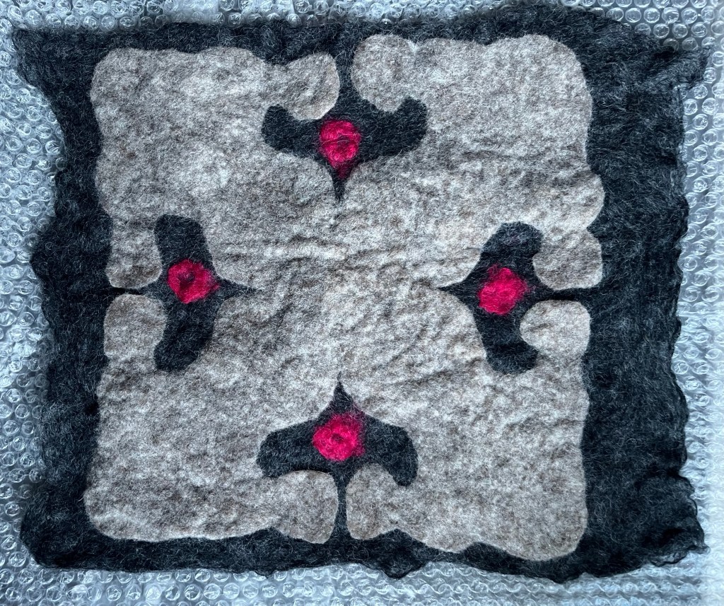 Details of Large felt collage with Persian carpet-inspired center, soft green wings, and ceramic elements, merging traditional patterns with symbolic forms of protection and flight.