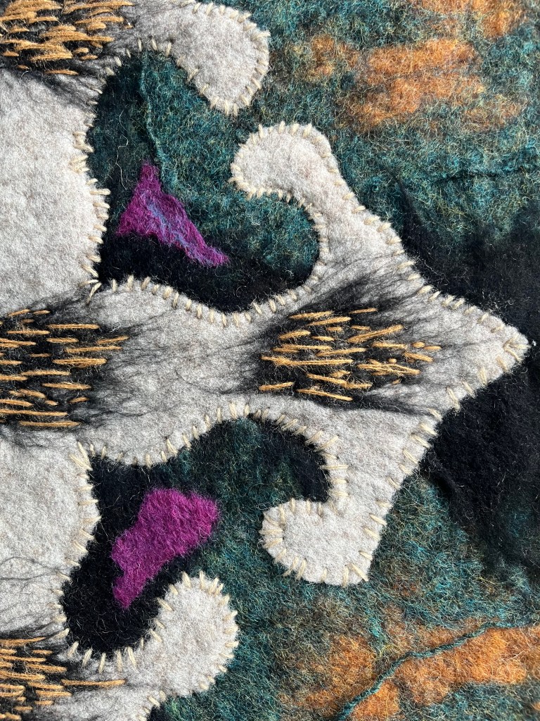 Details of Felt composition with a large ornamental motif in soft grey and black, set against a marbled background of dark green and amber tones, inspired by Persian design elements and textile tradition.