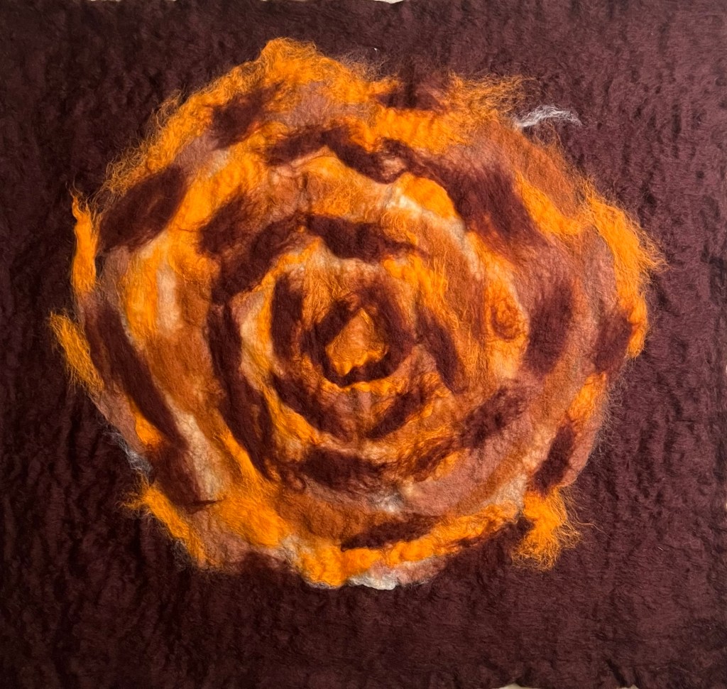 Concentric spiral of warm-toned wool—burnt orange, rust, and soft browns—radiating from a dark, central point on a deep aubergine felt background, resembling a glowing eye or a seismic bloom.